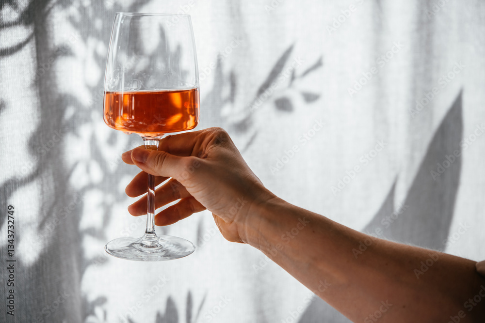 Hand holding a glass of rose wine in summer sunshine during a wine tasting in a bar or restaurant.