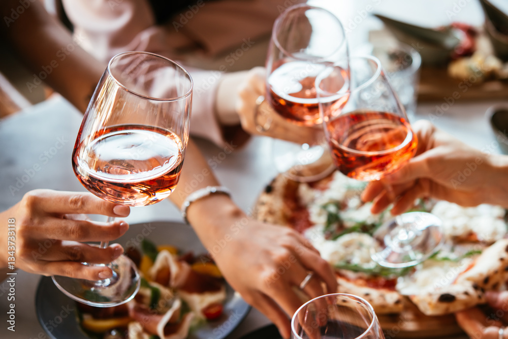 Friends enjoy a dinner party with pizza and rose wine in a bar or a restaurant.