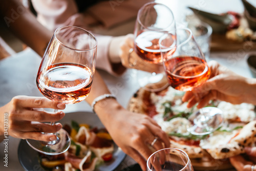 Friends enjoy a dinner party with pizza and rose wine in a bar or a restaurant.
