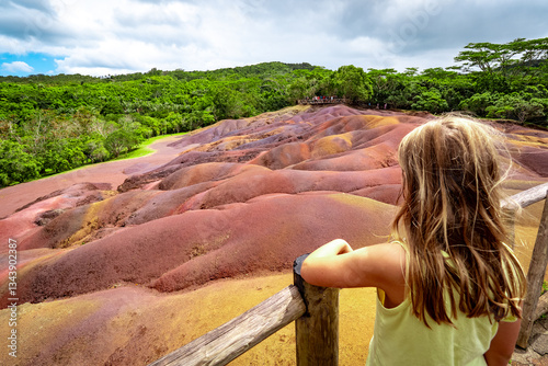 View of a young girl looking in fascination at the amazingly eroded colorful dunes at the Seven Colored Earth Geopark in Chamarel, Mauritius