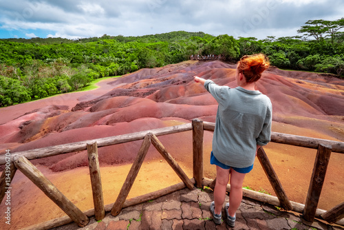 View of a woman looking at the amazingly eroded colorful dunes at the Seven Colored Earth Geopark in Chamarel, Mauritius, pointing with her finger