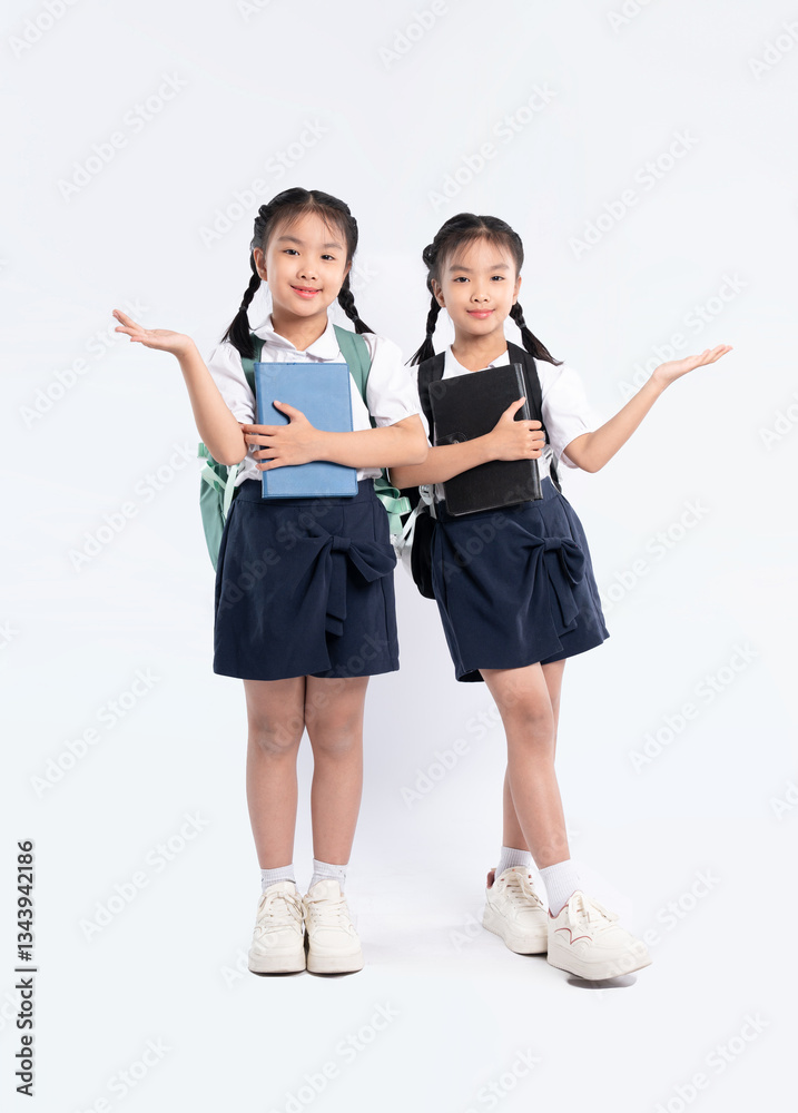 Naklejka premium Two young schoolgirls in uniform with books and backpacks present towards the camera on a white background