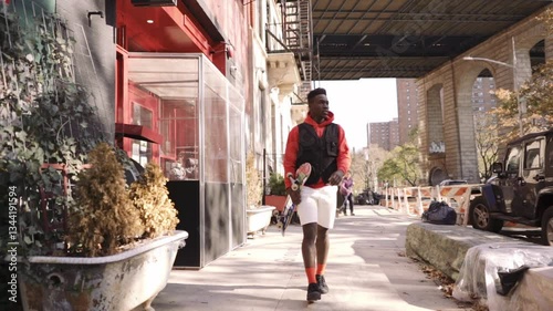 Young black male fashion model walking through the streets of New York City while grabbing his skateboard