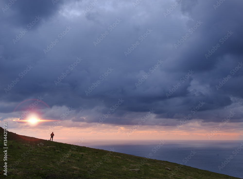 After the storm the sun comes out. Hiker on the Jaizkibel mountain in front of the sea, Basque coast.