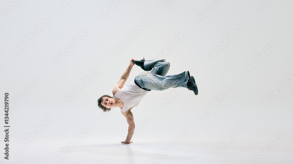 Skilled b-boy, dressed casually, executing powerful aerial move, seamlessly merging art and sport against white background. Concept of breakdance, music, contemporary movement, power, street dance. Skilled b-boy, dressed casually, executing powerful aerial move, seamlessly merging art and sport against white background. Concept of breakdance, music, contemporary movement, power, street dance.