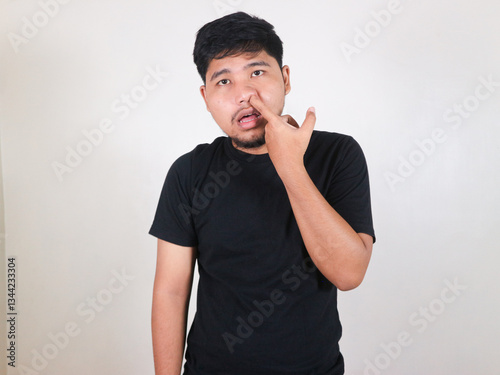 Handsome Asian man wearing black shirt is picking his nose to clean snot with an innocent expression