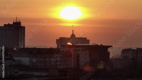 Pedestal drone rise revealing the Presidential Building of Chisinau with the flag on top, emerging from behind buildings against the sunrise in Moldova