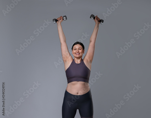 Obraz na płótnie Plus size woman in gym clothes doing exercise with dumbbells on grey background w salonie