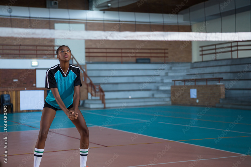 In school gymnasium, athlete preparing to receive volleyball with focus, copy space