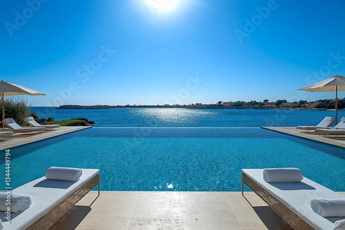 Stunning infinity pool overlooking a calm sea under a bright sun  with lounge chairs and towels.