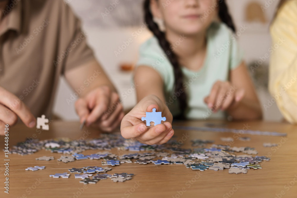 Parents and their daughter solving puzzle together at wooden table indoors, closeup Parents and their daughter solving puzzle together at wooden table indoors, closeup