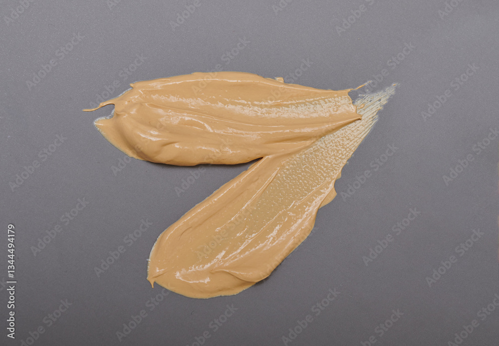 Light pale brown yellow gold color cosmetic cream texture. Lotion smear. Creamy skincare product swatch isolated gray background.