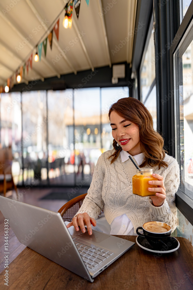 Freelancer enjoying orange juice and working on laptop in cafe Freelancer enjoying orange juice and working on laptop in cafe