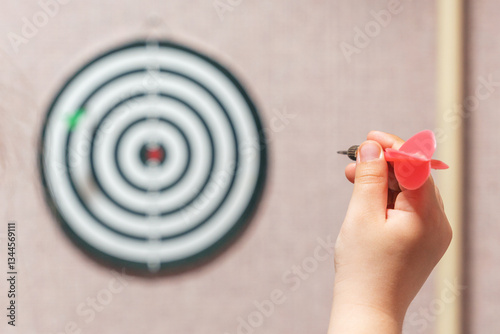 Playing darts, child's hand aiming a dart at a target