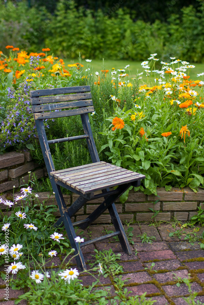 herb spiral in the garden with fresh herbs and flowers and old chair