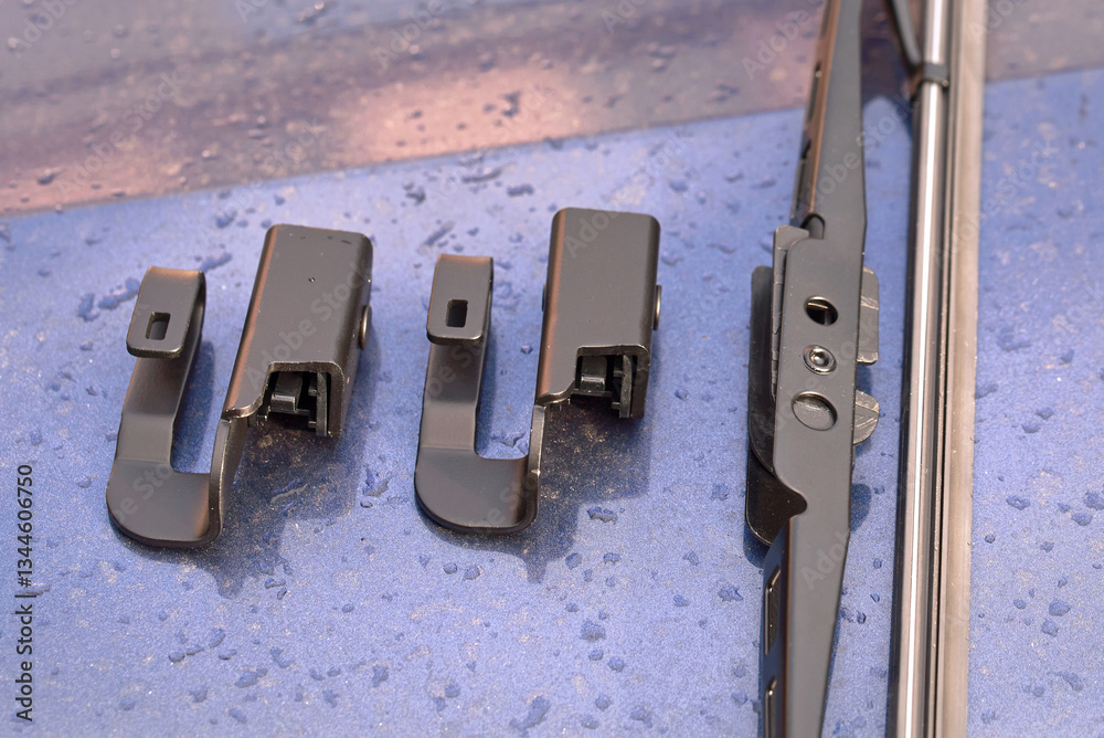 Wiper blade and adapter for offset axle installation on vehicles closeup. Wiper blade adapters on wet surface with water droplets, adapters for clear visibility in rainy or dusty road conditions