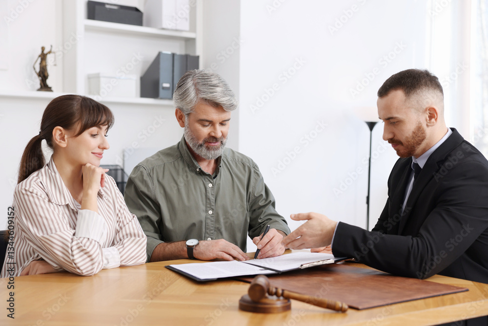 Clients signing notarial paperwork during meeting with lawyer at wooden desk indoors Clients signing notarial paperwork during meeting with lawyer at wooden desk indoors