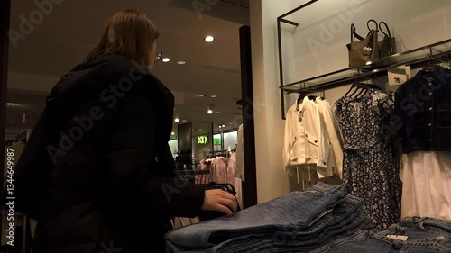 Russia, Moscow - March 19, 2025: woman browses clothing racks are full of various garments in store. scene is dimly lit, creating a shopping atmosphere