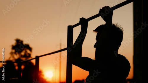 Teenage boy pulls himself up on horizontal bar in street training and sports yard among youth