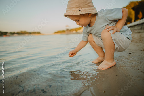 A two-year-old boy is playing on the shore of a city lake  