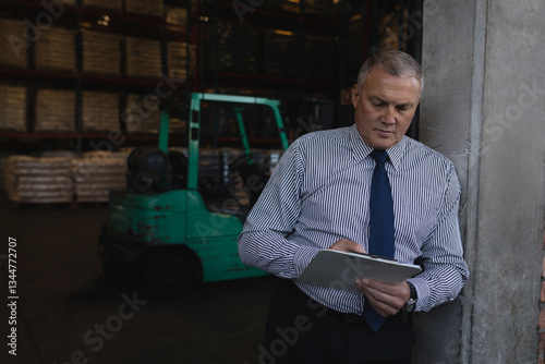 Businessman in warehouse writing on clipboard, focusing on inventory management, copy space