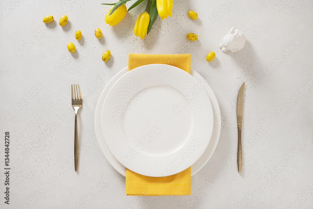Easter table setting with spring, yellow tulips, white plates, bunny, eggs on white background. Happy Easter celebration. Copy space. View from above.