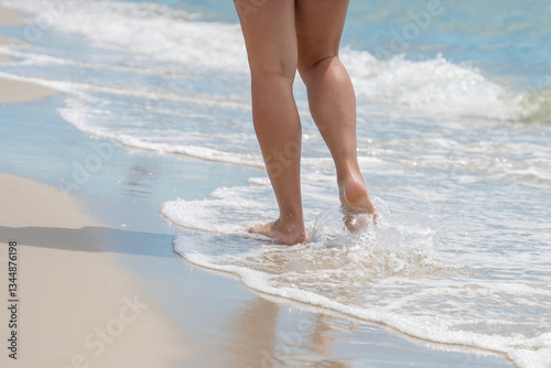 Canvas Print A girl walks along a sandy sea beach on a sunny summer day, sea water washes her