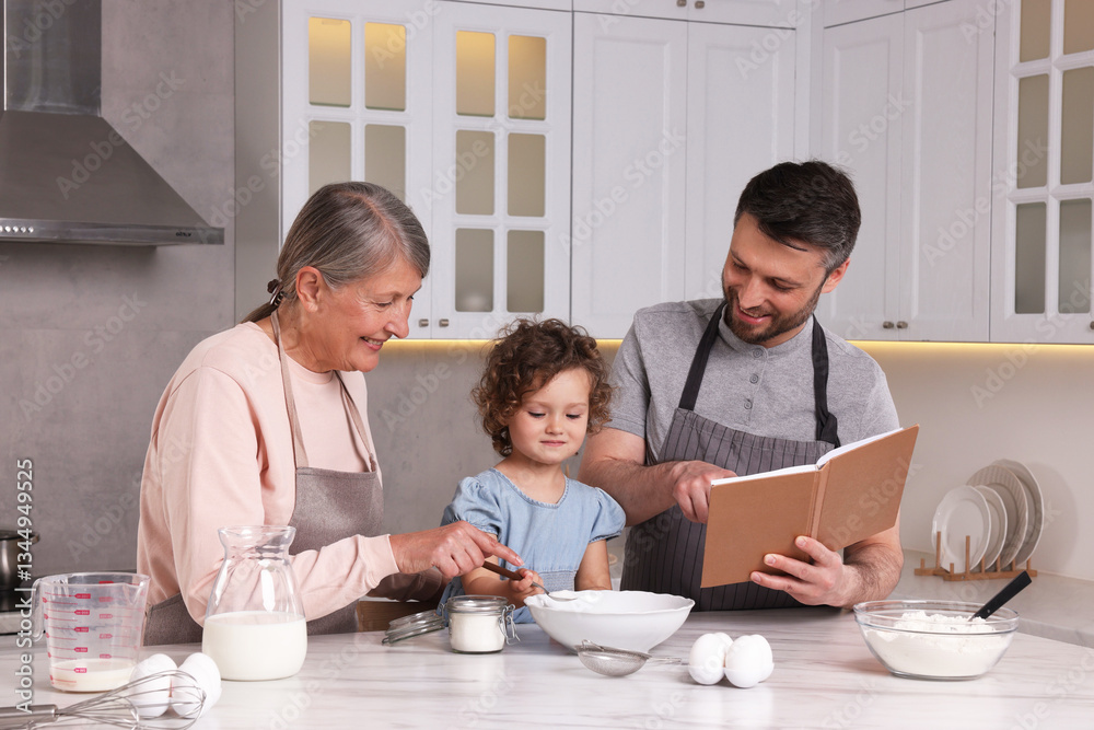 Cute little girl with her father and grandmother cooking by recipe book in kitchen Cute little girl with her father and grandmother cooking by recipe book in kitchen
