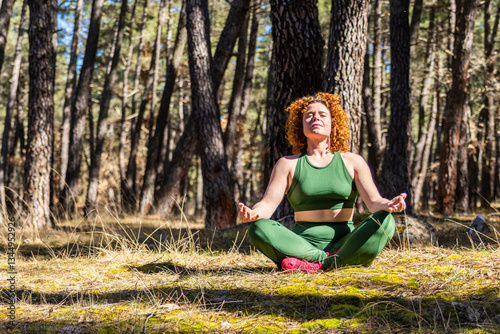 Redhead woman meditating in green suit in a pine forest photo