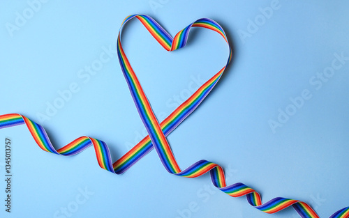 Vibrant rainbow ribbon shaped into a heart on soft blue background for celebration of love and diversity.LGBT, LGBTQ, gay pride month .