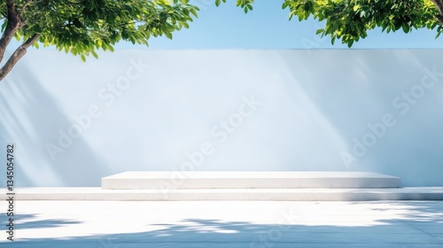Outdoor, light gray platform, bathed in sunlight, with lush greenery and a pale blue wall