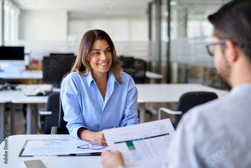 Smiling mature female financial advisor, professional bank manager consulting client working in corporate office. Happy middle aged business woman hr talking to recruit at job interview meeting.