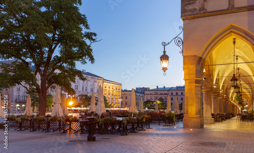 Obraz na płótnie Evening view of the Main Square in Krakow, Poland, featuring the illuminated arcade of the Cloth Hall and outdoor cafes with closed umbrellas w salonie