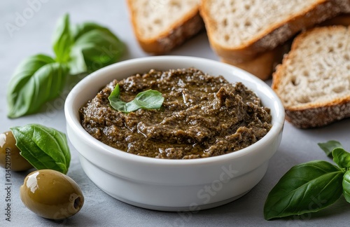 Fresh Olive Tapenade with Basil Leaves, Slices of Artisan Bread, Green Olives, and Natural Ingredients on a Gray Background for Gourmet Cuisine