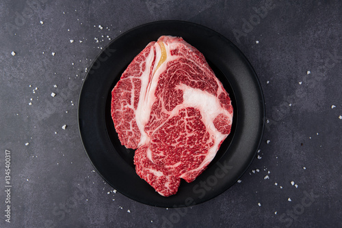 Raw fresh marbled beef steak on black plate with sea salt, top view
