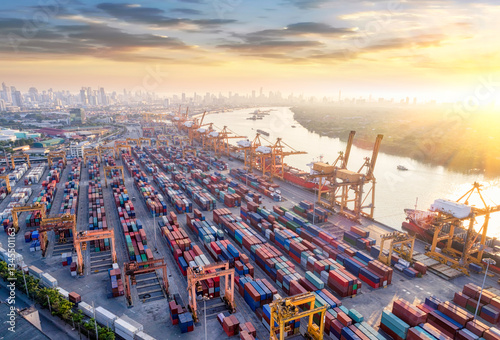 Aerial view and top view cargo Logistics and transportation of Container Cargo ship and Cargo plane with working crane bridge in shipyard at sunrise, logistic import export and transport 