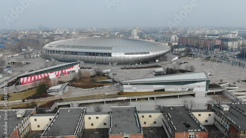 Modern sports arena with sleek metallic roof, surrounded by urban architecture and infrastructure in Budapest, Hungary, cityscape. Aerial drone view