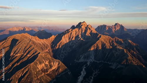 Sweeping Vista of Jagged Mountain Peaks Bathed in Golden Light at Sunrise with Hues of Orange and Blue Sky Backgrounds