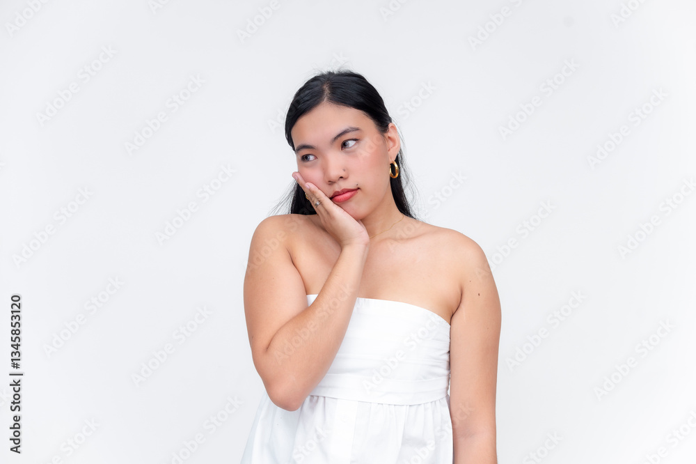 Asian woman with contemplative expression wearing white dress against isolated white background. Feeling worried. Asian woman with contemplative expression wearing white dress against isolated white background. Feeling worried.