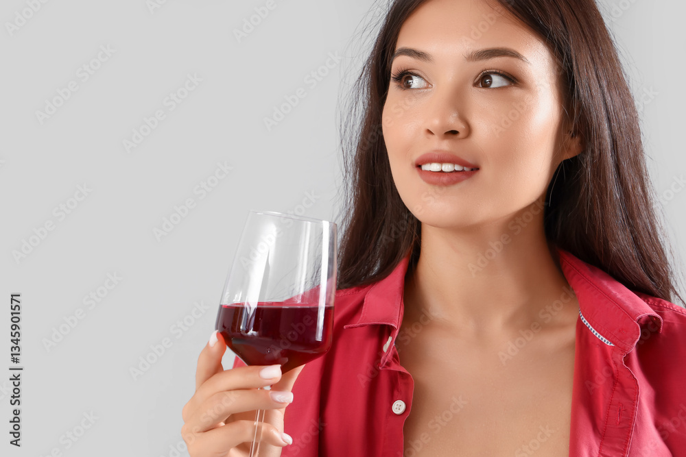 Beautiful young Asian woman with glass of wine on grey background Beautiful young Asian woman with glass of wine on grey background