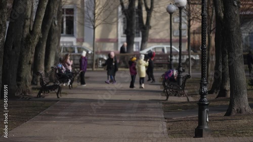 Wallpaper Mural Many children are walking in a city park on a sunny spring day. Focus on the foreground, blurred school children are walking along a pedestrian path in the park among benches and trees. Torontodigital.ca