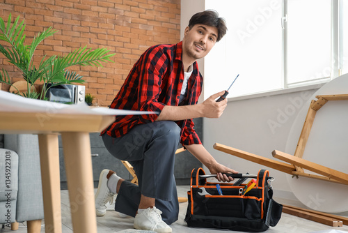Male worker with bag of tools assembling furniture in kitchen
