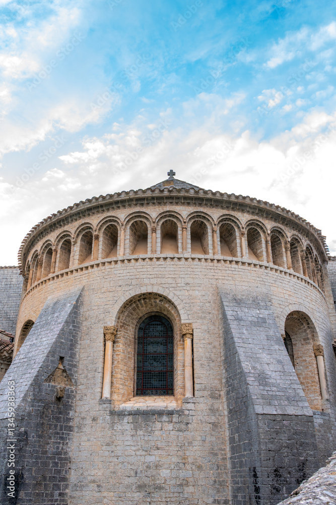 Obraz premium Ancient Romanesque church with arched windows and stone walls, featuring a stained-glass window, buttresses, and a blue sky