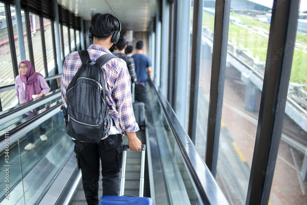 Obraz premium Rear View Of Collage Student Man Moving Down While Carrying Suitcase On Escalator In Train Station