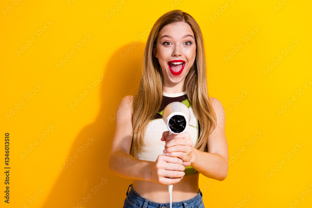 Obraz premium Happy young woman holding a hairdryer in colorful casual outfit against a bright yellow background