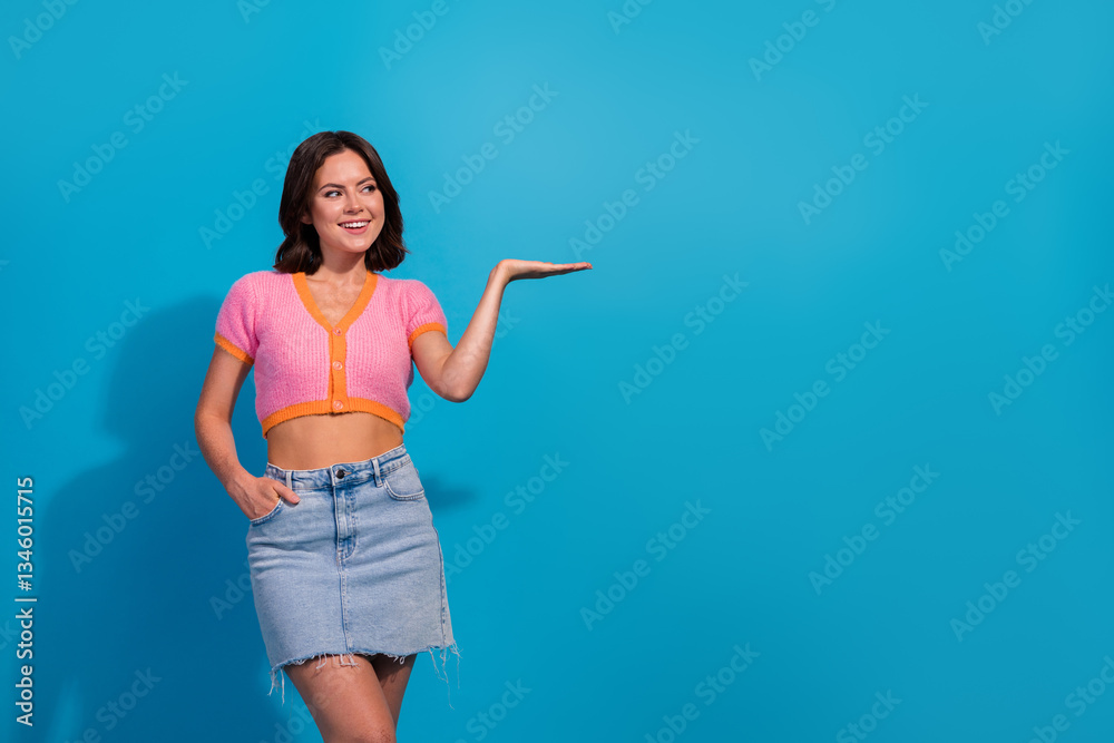 Smiling young woman in casual summer outfit gesturing with one hand against a vibrant blue background Smiling young woman in casual summer outfit gesturing with one hand against a vibrant blue background