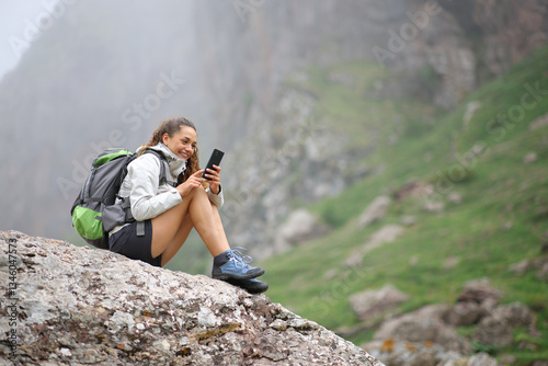 Happy hiker using smart phone sitting on a rock in nature