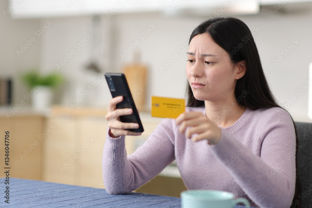 Sad asian woman paying online with card and phone at home Sad asian woman paying online with card and phone at home