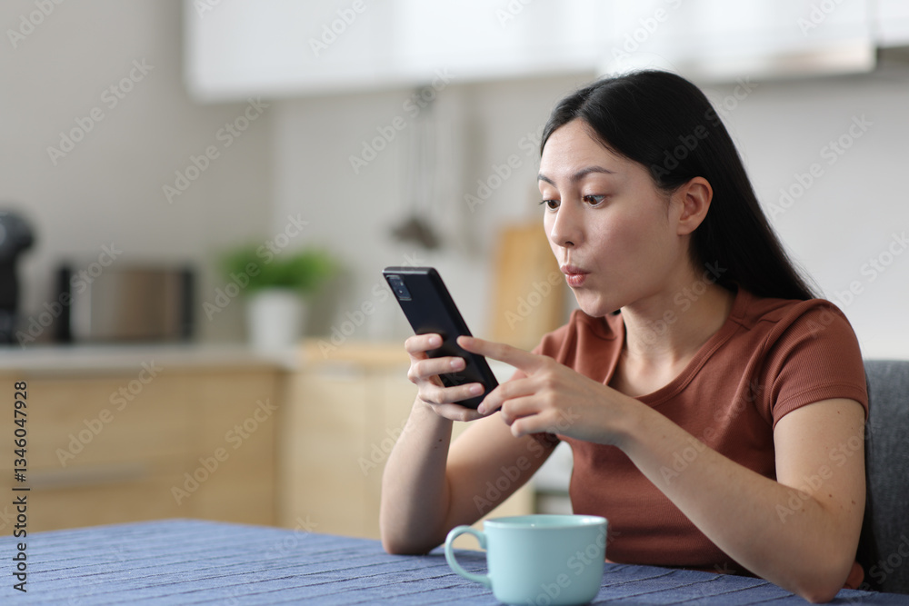 Surprised asian woman using smart phone in a kitchen Surprised asian woman using smart phone in a kitchen