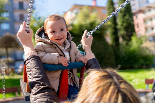 Schilderij op canvas Happy baby boy swinging at the playground with mother pushing